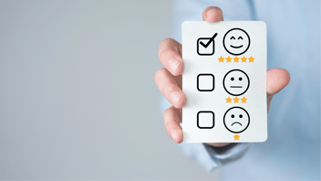 close up of hand holding up rating card with three different faces, the one smiling is checked